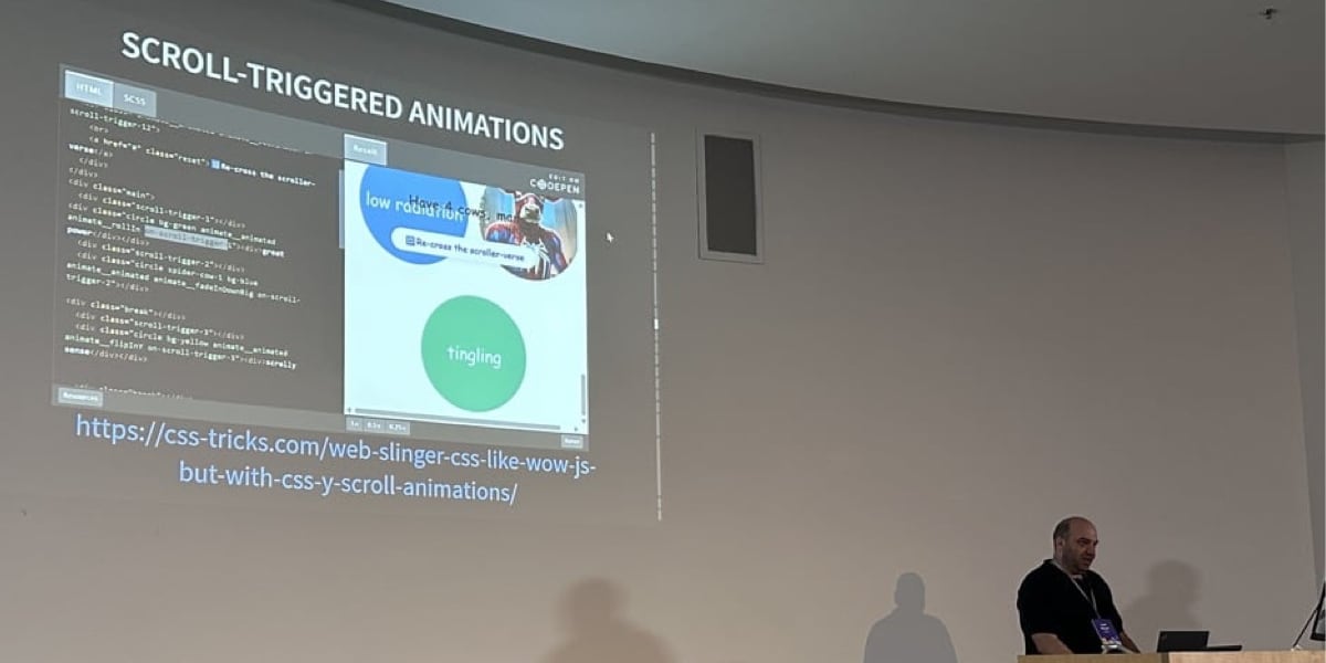 Lee Meyer speaking at light wooden lectern in front of a projection showing a demo of his scrollytelling library on CodePen.